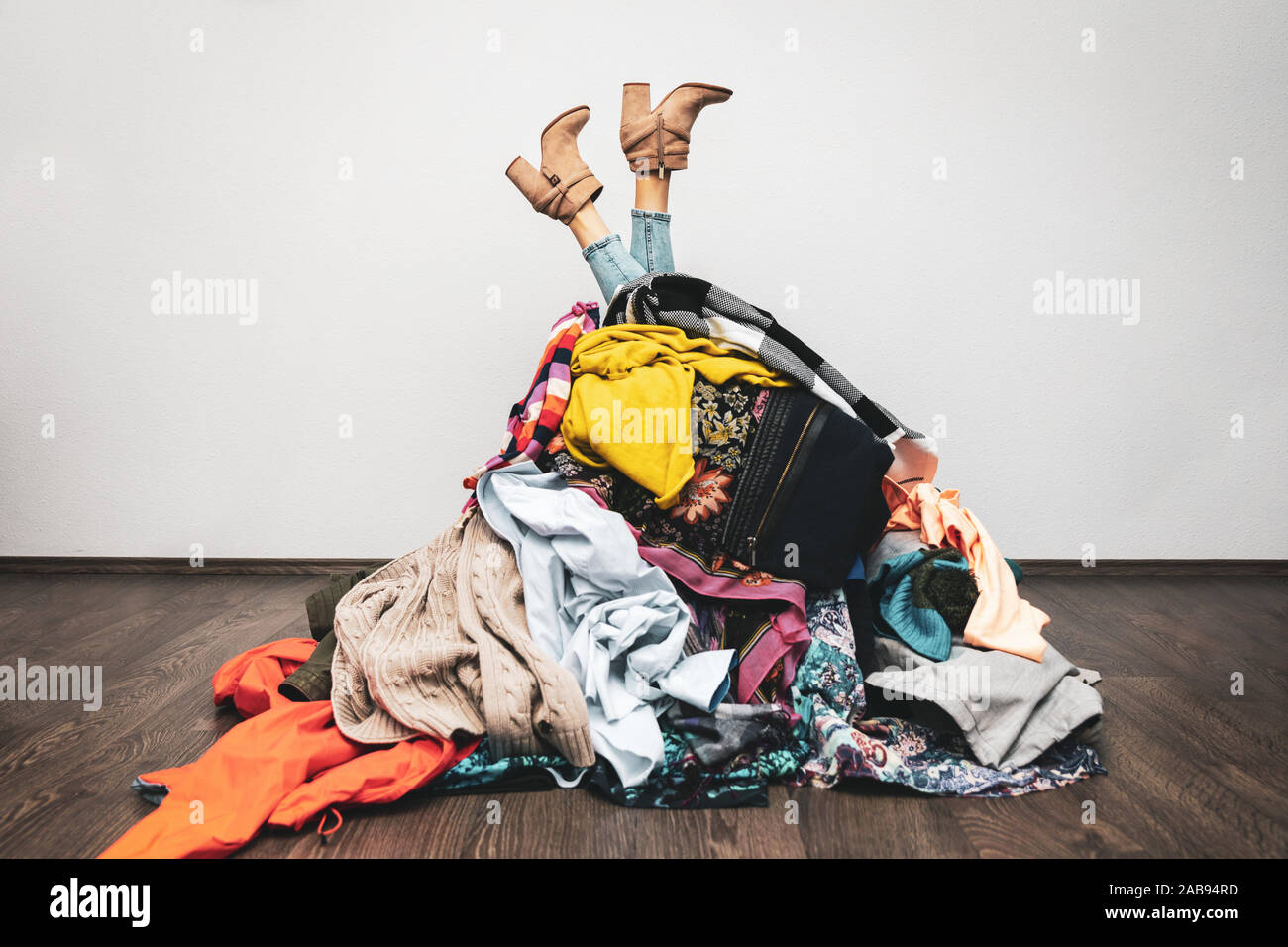Frau Beine aus einem Stapel von Kleidung auf dem Boden. kaufsucht Konzept Stockfoto