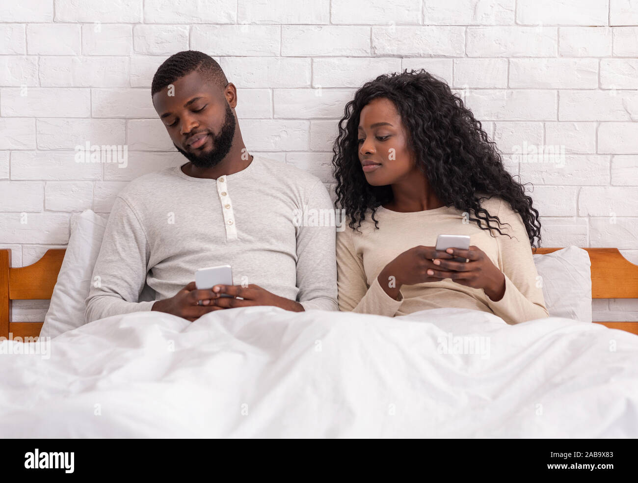 Eifersüchtig Spähen in's Frau Handy sitzen auf dem Bett zusammen Stockfoto
