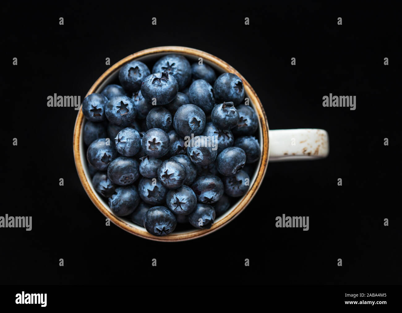 Frische Heidelbeeren in einer Tasse auf einem schwarzen Hintergrund. Ansicht von oben, Makro. Blaue reife Beeren Nahaufnahme. Essen Hintergrund. Stockfoto