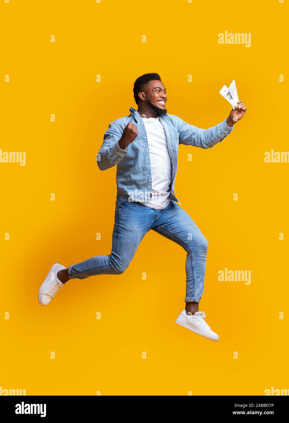Euphorisch afro Mann springen mit Bargeld in der Hand auf gelbem Hintergrund Stockfoto