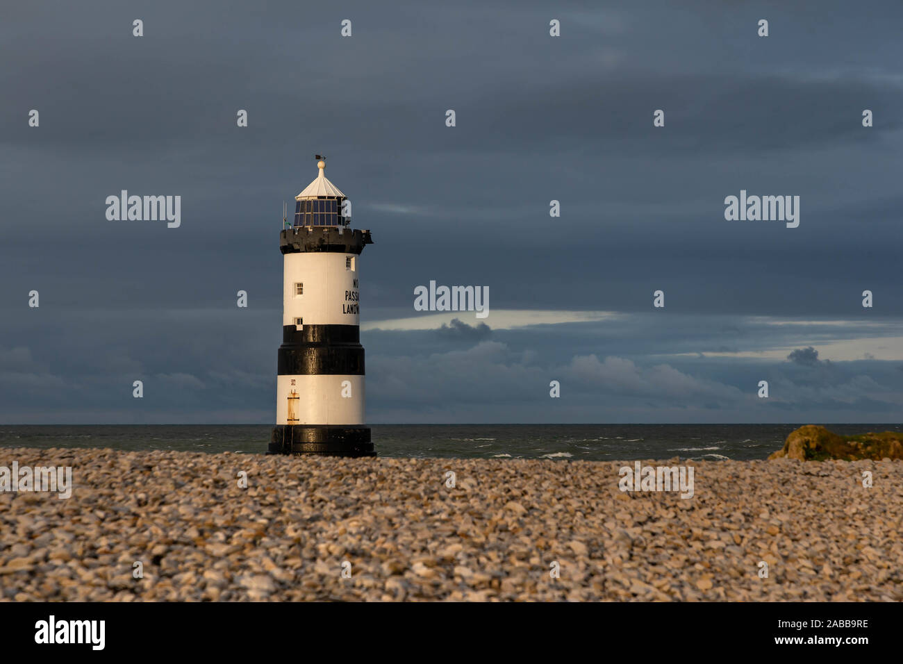 Du Trwyn penmon Leuchtturm (Leuchtturm) auf der östlichen Extremität von Anglesey, Nordwales, mit einem Strahl der Sonne durch die Gewitterwolken brechen Stockfoto