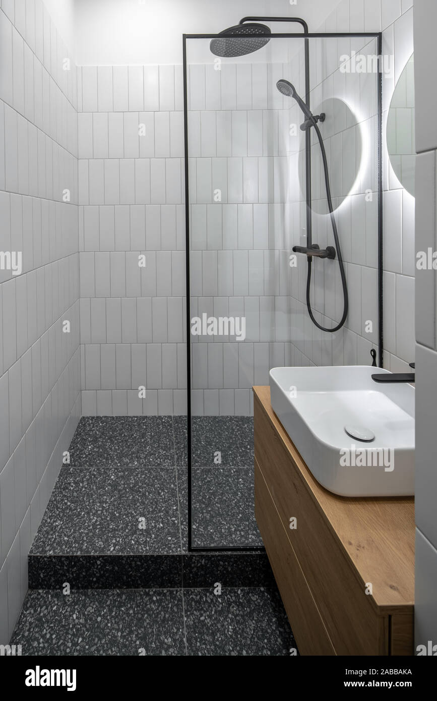 Stilvolle helle Badezimmer mit Fliesen- weiße Wände und texturierte  Dunkelgrau Stock. Es gibt eine schwarze Dusche, Glaswand, runder Spiegel  mit Hintergrundbeleuchtung Stockfotografie - Alamy