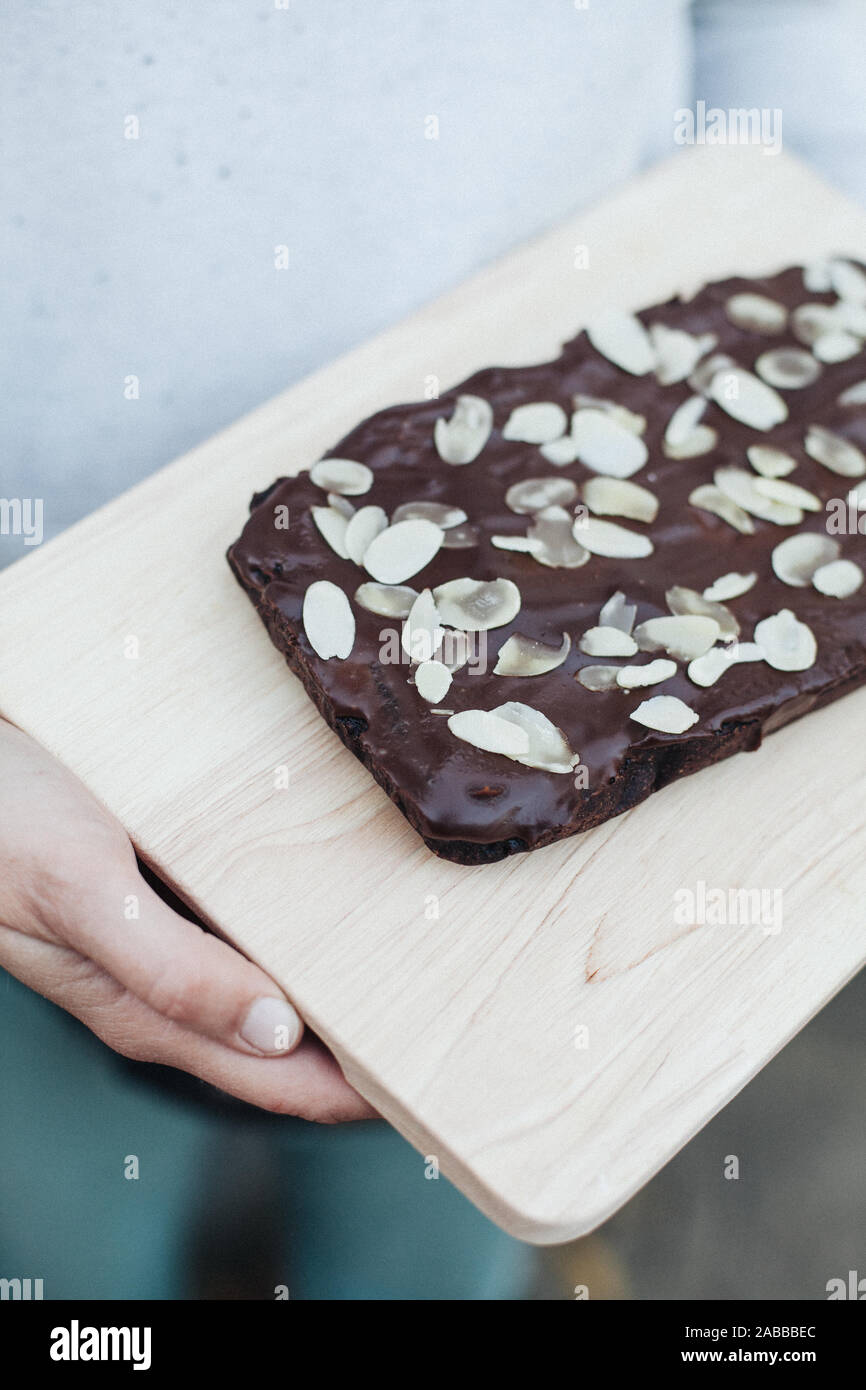 Frau mit einem Schneidbrett mit eine Gesunde vegane Schokolade und Mandel Brownie Stockfoto