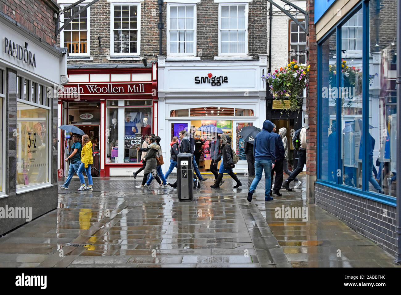 Fußgänger wandern im Regen auf dem nassen Einkaufsstraße Pflaster außen Smiggle Australische retail Chain Store Schreibwaren business Durham England Großbritannien Stockfoto