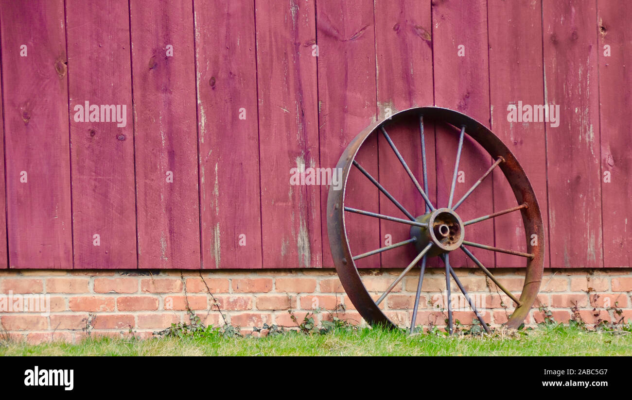 Antike landwirtschaftliche Traktor Rad lehnte sich gegen rote Scheune Beplankung. Stockfoto