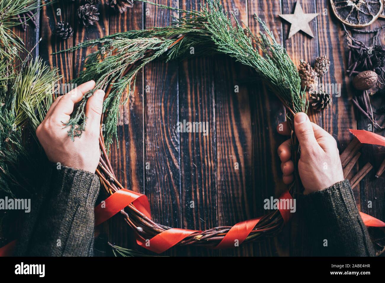 Männliche Hände machen Weihnachten Kranz mit Tannenbaum brunches auf dunklen Hintergrund Stockfoto