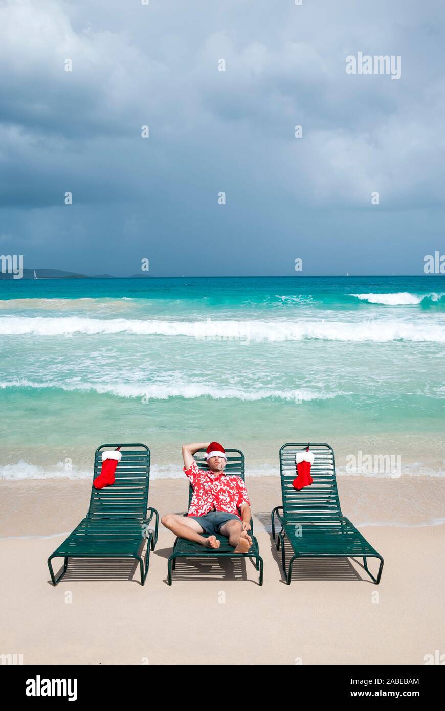 Mann in Santa Hut und passenden Urlaub aloha Shirt entspannen im Strandkorb neben Weihnachten Strümpfe Stockfoto