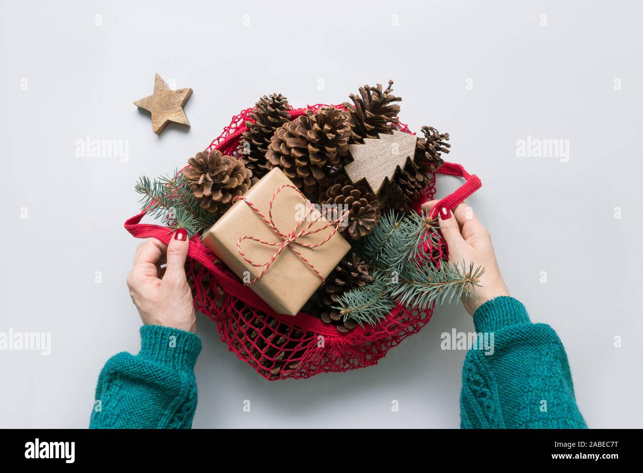 Frau Hände halten Netzbeutel mit Weihnachten null Abfall Einrichtung, nachhaltige Geschenk, Kegel und Tannenbaum Niederlassungen für handmade Design. Umweltfreundliche Weihnachten. Stockfoto