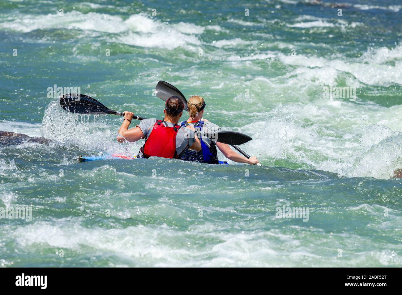 Frauen Paare im Kanu Rennen hinten Aktion Foto des Flusses Felsen Rapids mit paddlern durch hetzende rauhen Gewässern. Stockfoto
