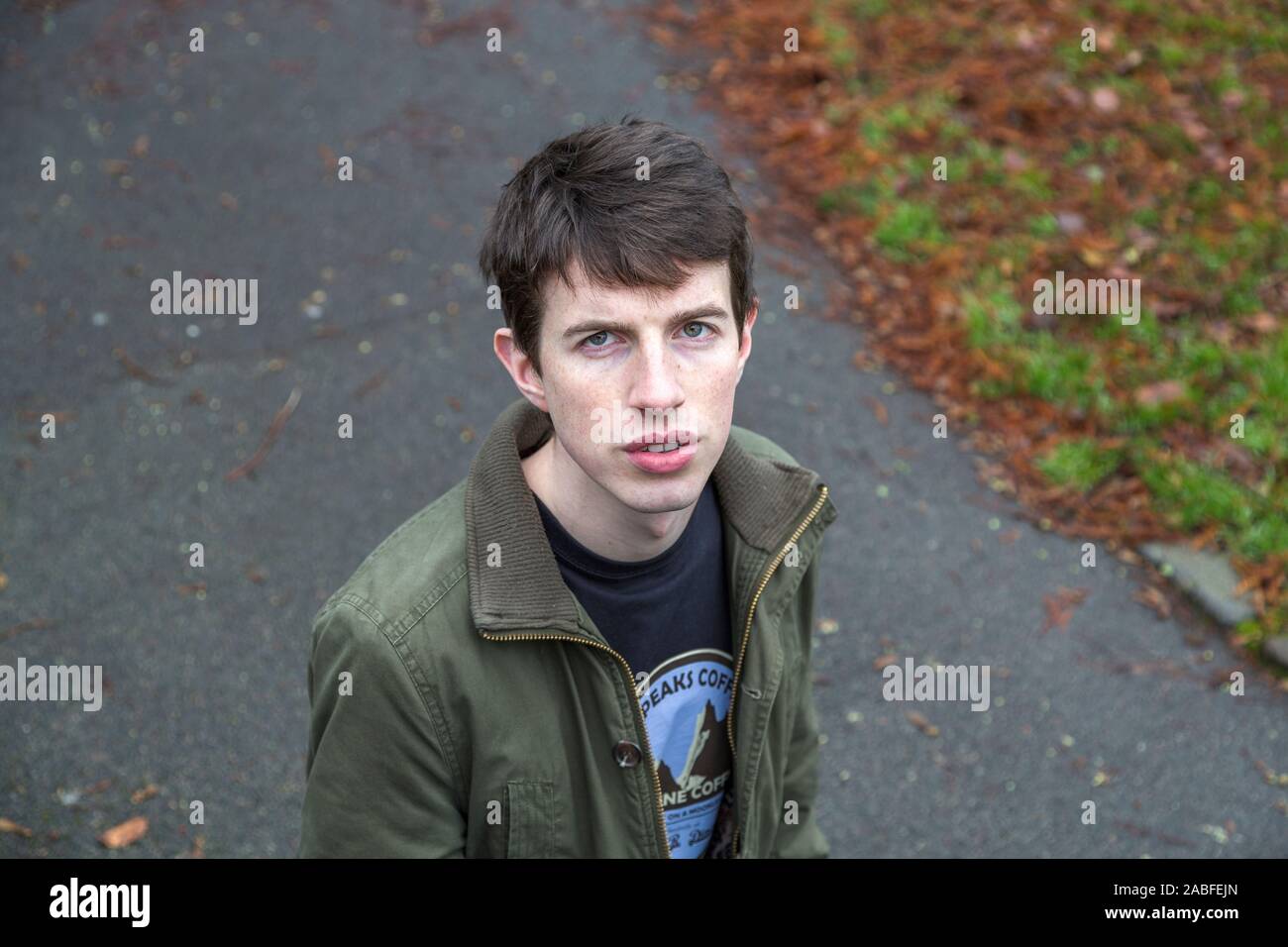 Einen attraktiven jungen Mann in seinen späten Teens oder Anfang der 20er Jahre steht in einem Park bis in die Kamera schaut. Stockfoto