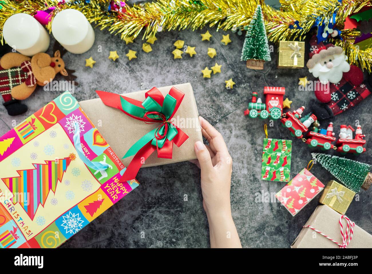 Hand mit Geschenk Box von Shopping Bag während der Weihnachtszeit und Geschenk Festival, Dekorationen mit Christmas Ornament auf Tisch Stockfoto