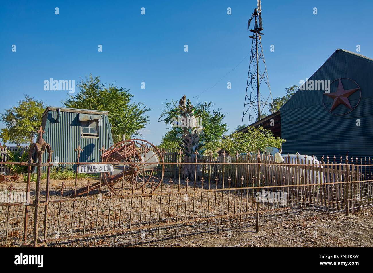 Eine Vorsicht vor dem Hund Schild auf der Gusseisen verrostete Zaun eines Garten eines Hauses ist, mit einer Metall Pferd angetriebenen Kutsche antik im Hof, und eine Dose werfen. Stockfoto