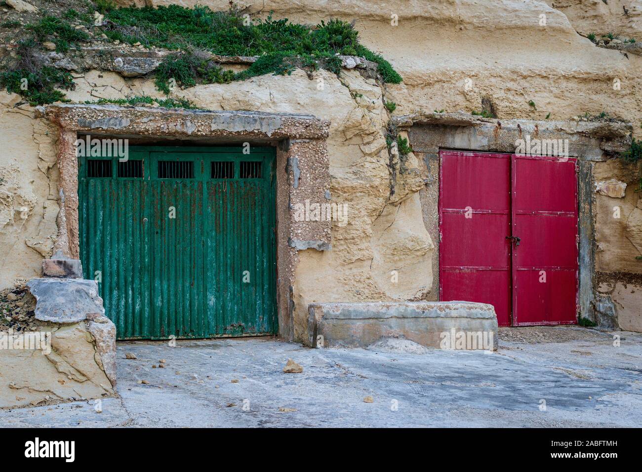 Das Fischerdorf Dahlet Qorrot auf der Insel Gozo, Malta. Bootshaus aus den weichen Kalkstein Klippe. Grün und rot Holz lackiert Türen. Stockfoto
