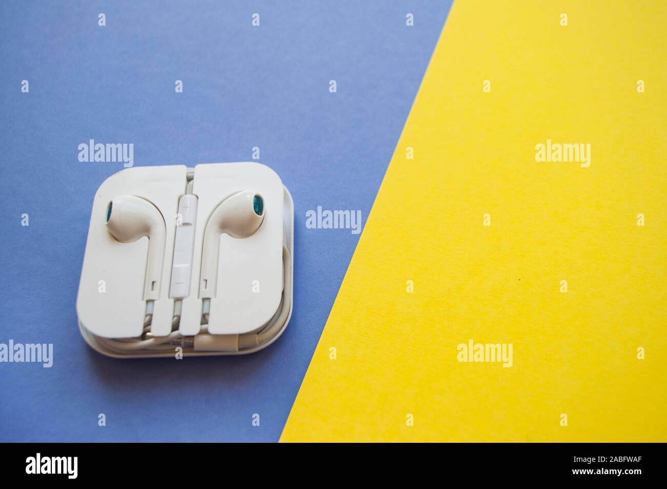 Ohrhörer in ein weißes Kunststoffgehäuse auf einem hellen Gelb, Rosa und blauen Hintergrund. Stockfoto