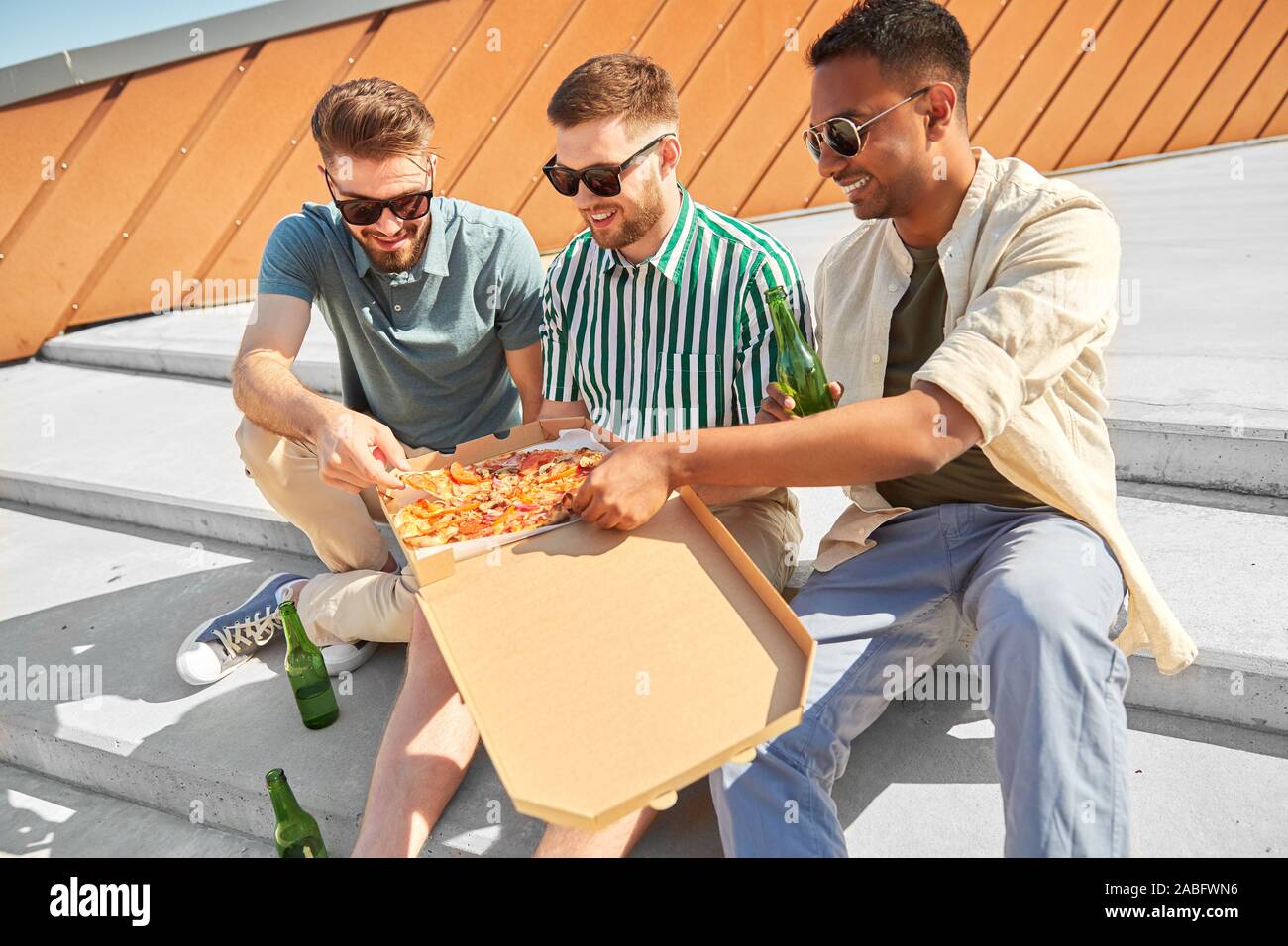 Männliche Freunde essen Pizza mit Bier auf Treppen Stockfoto