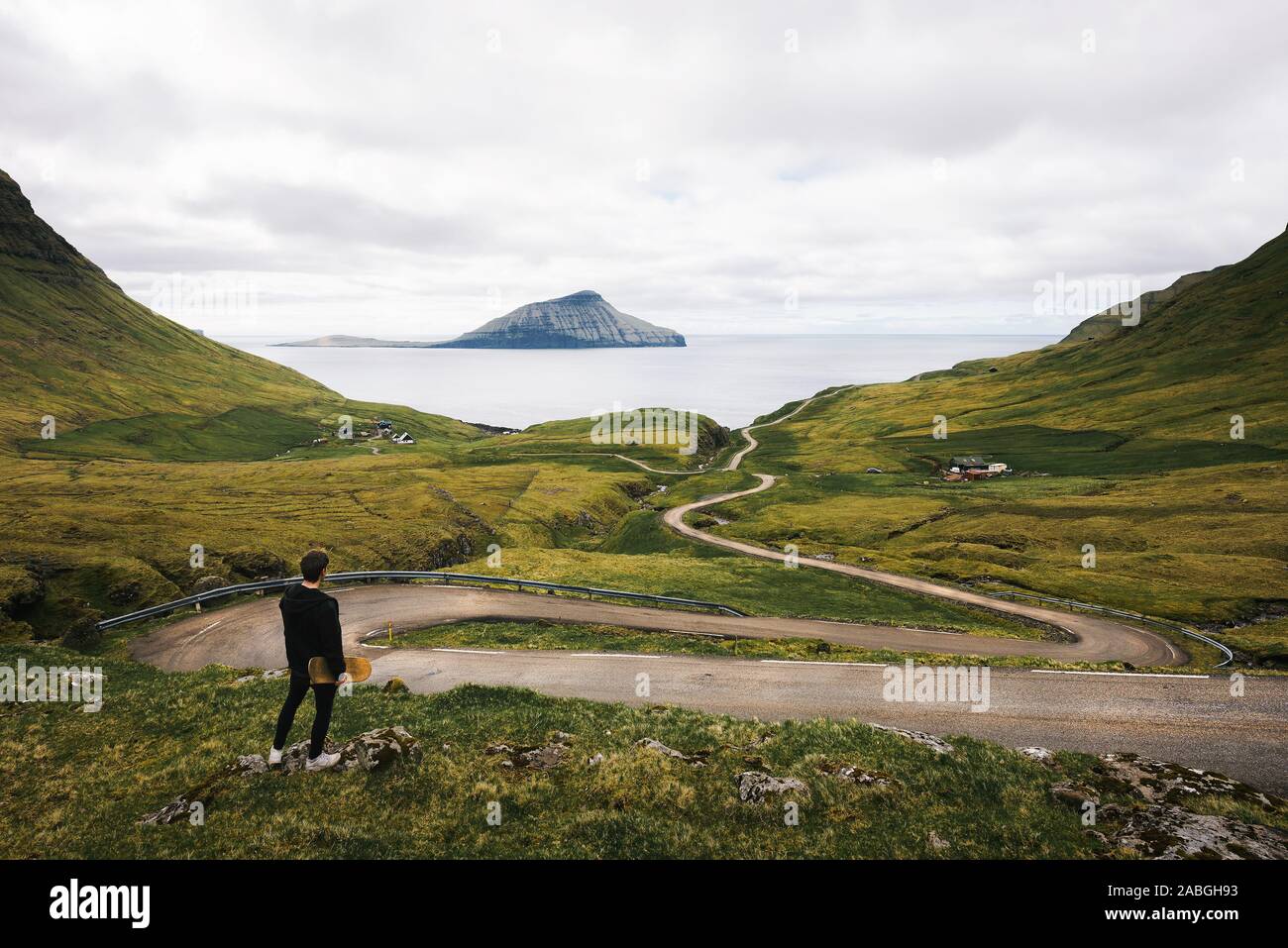 Jungen Skater mit seinem Skateboard schaut auf eine kurvenreiche Straße auf den Färöer Inseln Stockfoto