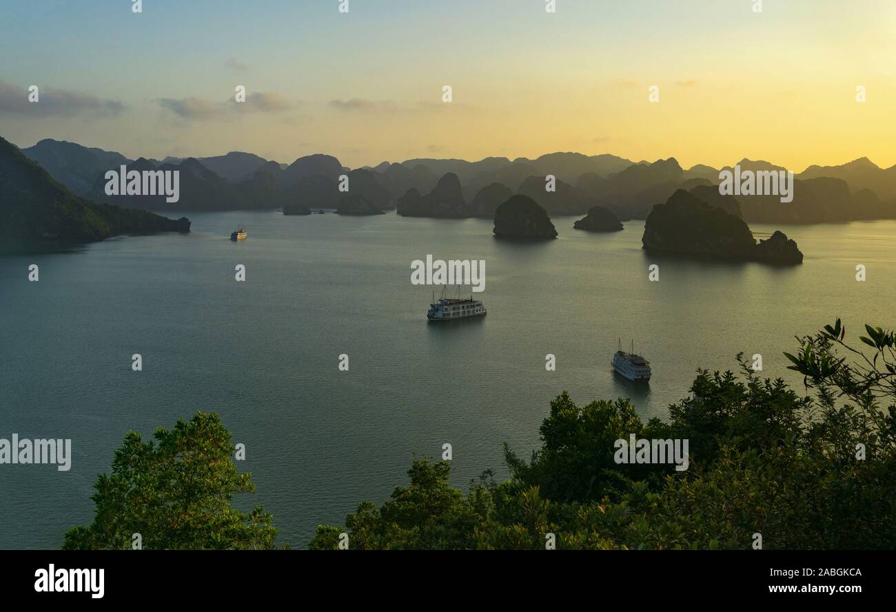 Drei Schiffe segeln zwischen den Inseln der Halong Bucht bei Sonnenuntergang Stockfoto