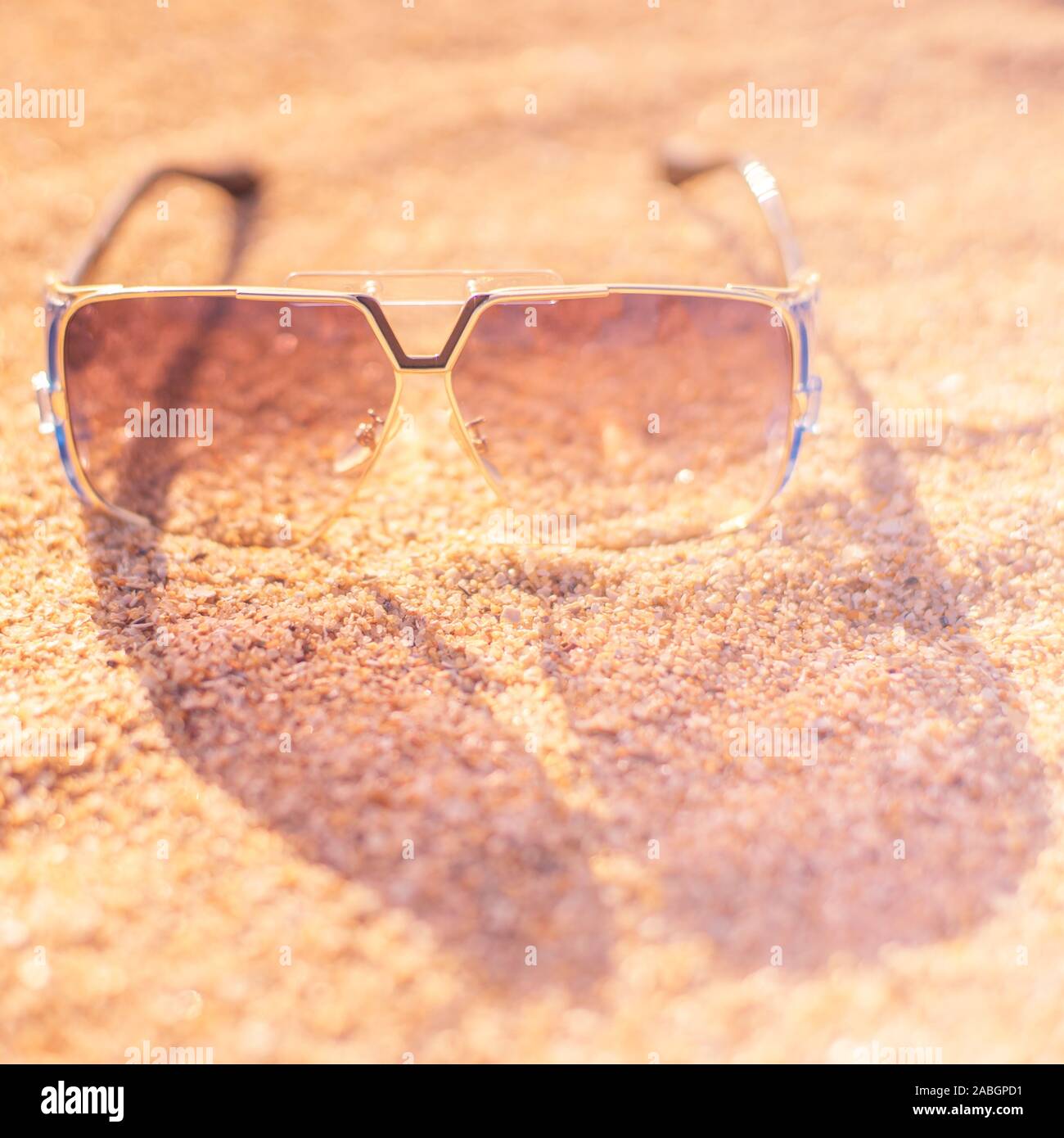 Stilvolle Sonnenbrillen liegen auf einem Sandstrand, transparentes Glas, Licht und Schatten. Stockfoto