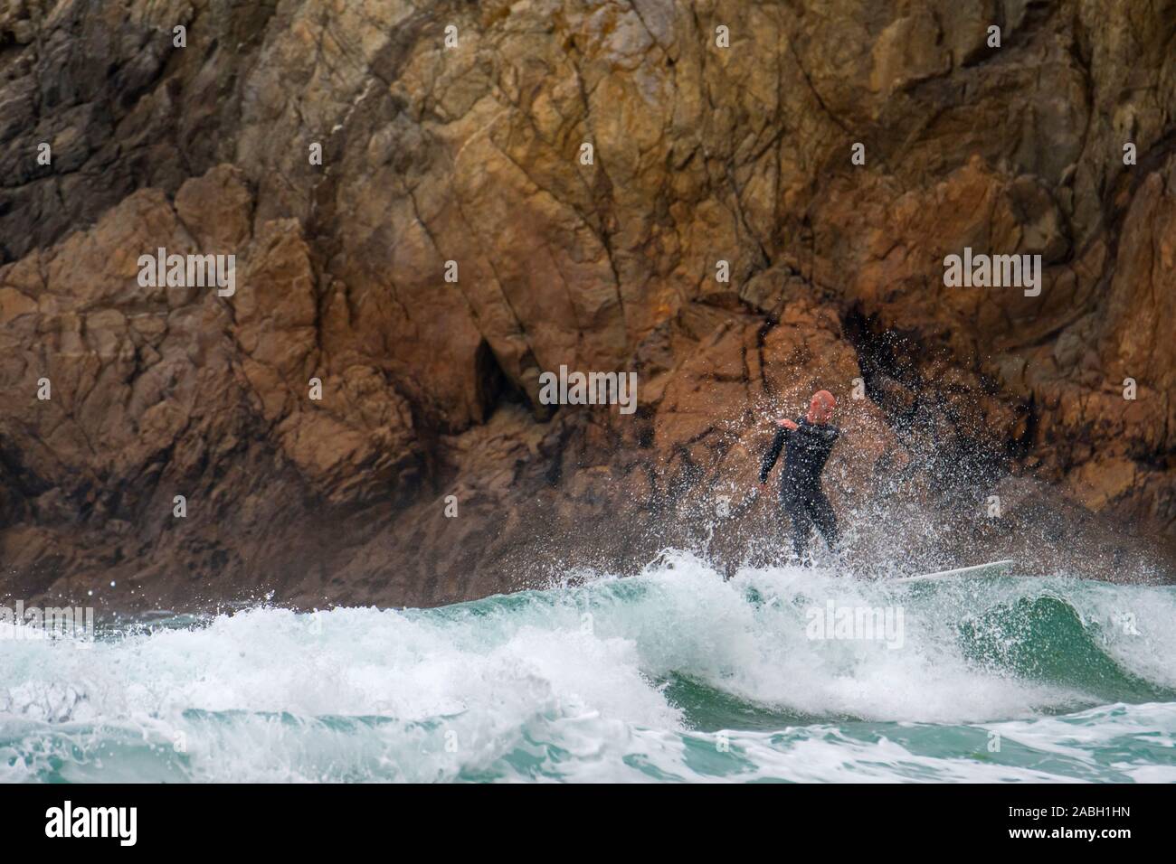 In Neoprenanzug Surfer Reiten eine Welle auf Surfboard gefährlich nah an die Felsen von Sea Cliff an der Pointe du Raz, Finistère, Bretagne, Frankreich Stockfoto