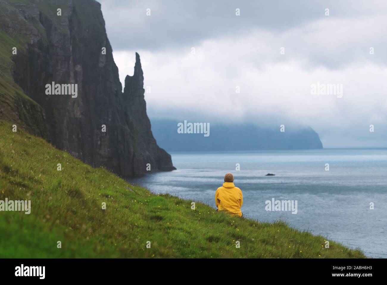 Touristen in der gelben Jacke sieht sich Hexen Finger Klippen von Trollkonufingur Aussichtspunkt. Vagar Island, Färöer, Dänemark. Stockfoto