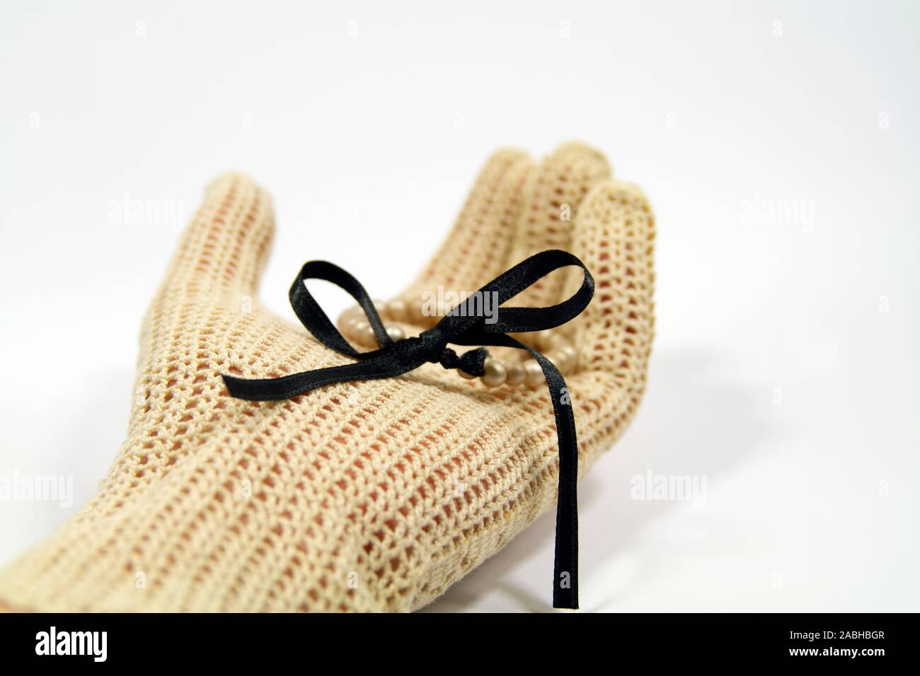 Hand mit Vintage gestricken Handschuh holding Perle Armband mit schwarzem Satinband Stockfoto