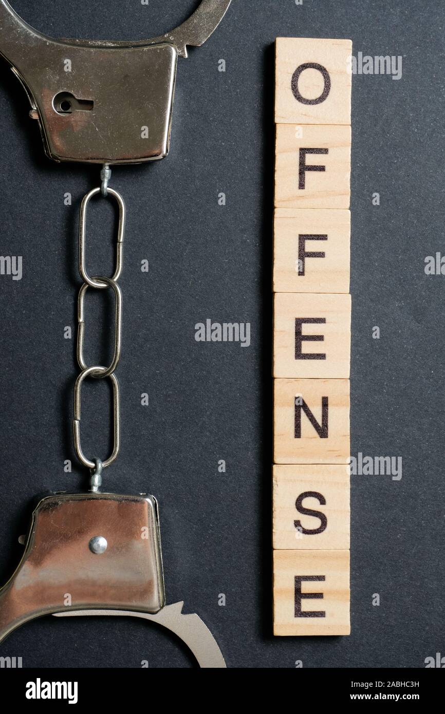 Ein Wort aus Holz Buchstaben ist eine Straftat. Handschellen aus Metall auf einem schwarzen Hintergrund. Das Konzept der das Gesetz zu brechen. Close Up. Ansicht von oben. Stockfoto