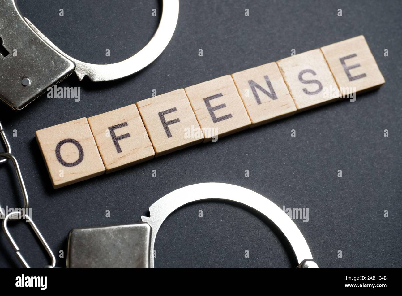 Ein Wort aus Holz Buchstaben ist eine Straftat. Handschellen aus Metall auf einem schwarzen Hintergrund. Close Up. Stockfoto