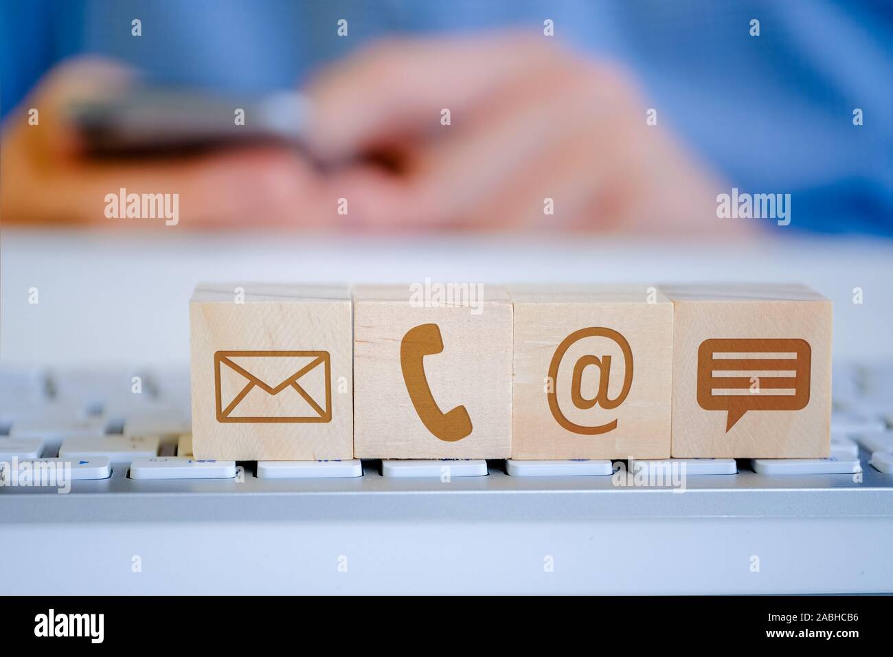 Ein Mann hält ein Smartphone mit seinen Händen, im Vordergrund Es gibt Holz- Würfel mit Buchstaben, E-Mail-, Telefon- und Nachrichtensymbole. Das Konzept der Anzeigen Stockfoto