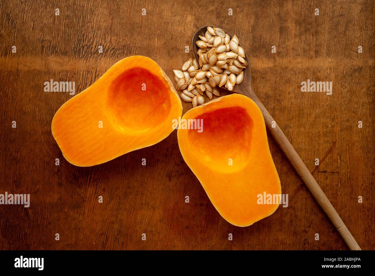 Zwei Hälften reifer Butternusskürbis mit Samen und altem Holzlöffel auf rustikalem Tisch von oben Stockfoto