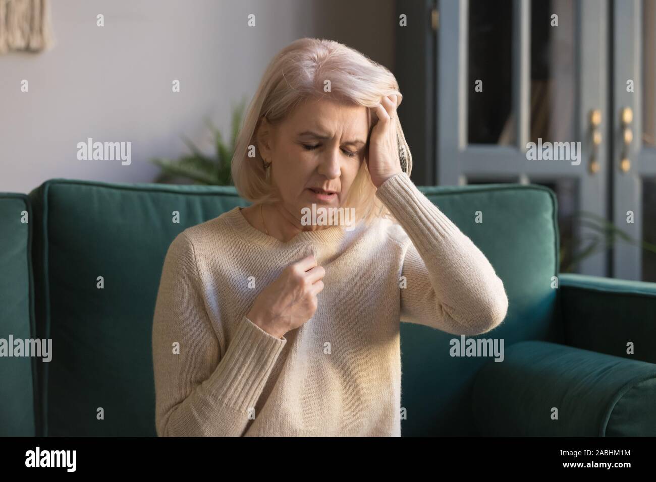 Reife Frau sitzen auf der Couch berührt Kopf fühlt sich ungesund Stockfoto