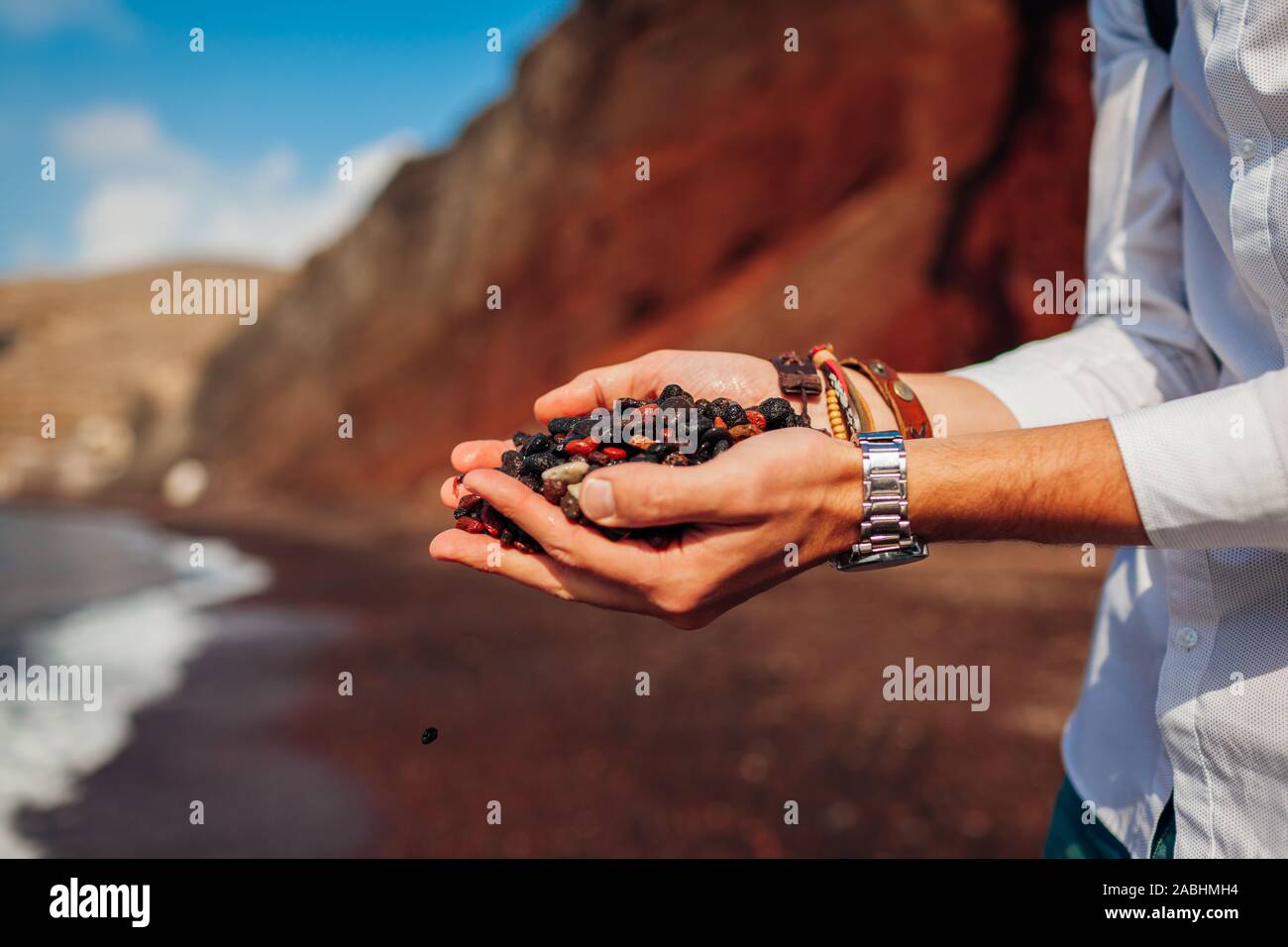 Red Beach Sand. Die Insel Santorini reisende Mann hält Handvoll Erde, kleine Steine in Chania, Griechenland. Stockfoto