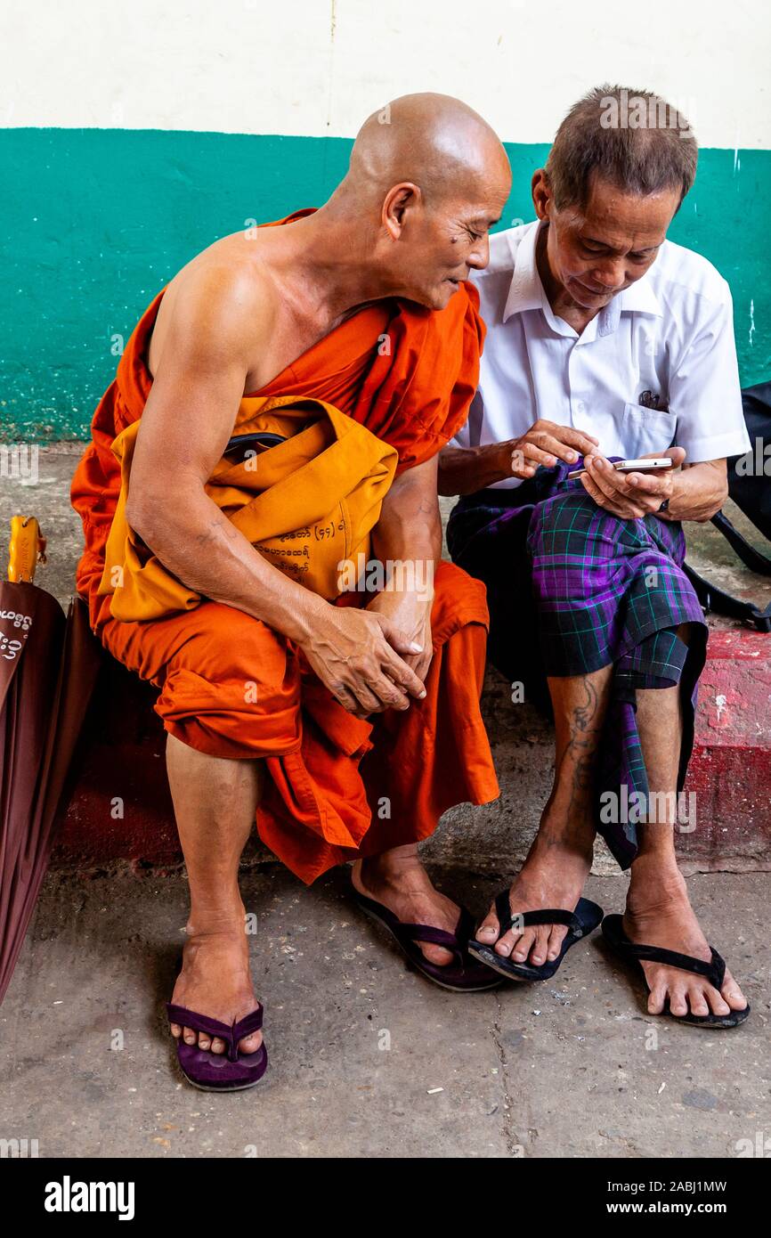 Ein buddhistischer Mönch und lokaler Mann Plaudern auf der Plattform eines Bahnhof, Yangon, Myanmar. Stockfoto
