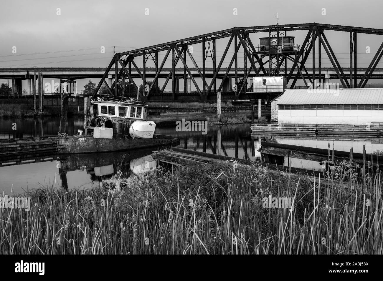 Alten, verlassenen Tug Boat in industriellen Marina mit train trestle im Hintergrund in Schwarz und Weiß. Stockfoto