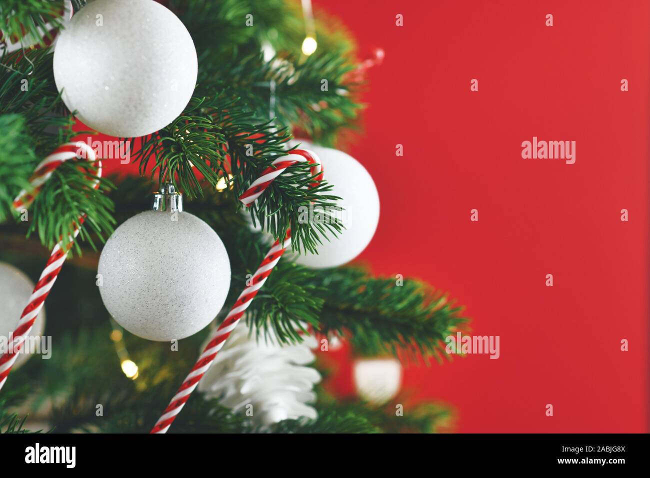 Nahaufnahme von geschmückten Weihnachtsbaum mit weißen und roten saisonale Baumschmuck wie Kugeln und Zuckerstangen auf rotem Hintergrund Stockfoto
