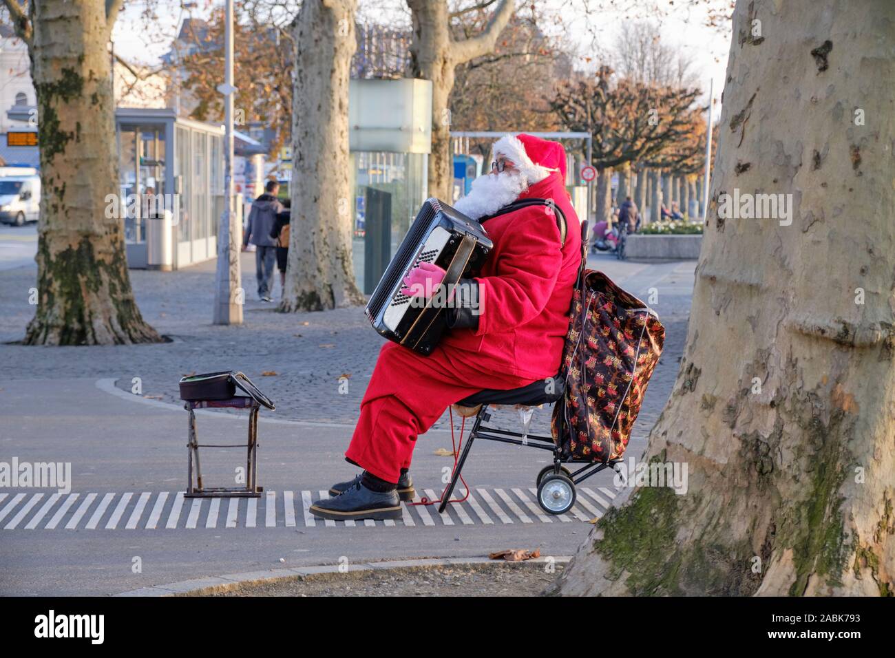 Seitenansicht des Street Performer in der Weihnachtsmann Kostüm sitzen, spielen auf dem Akkordeon. in Zürich, Schweiz Stockfoto