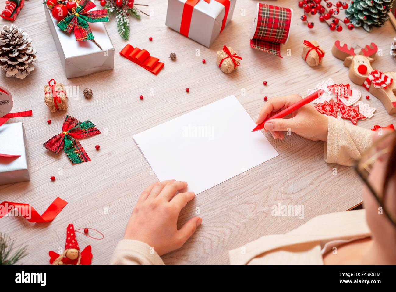 Mädchen schreibt auf Papier durch viele Weihnachten Geschenke und Dekorationen umgeben. Papier leer ist, Hinzufügen Grußkarte Text. Stockfoto