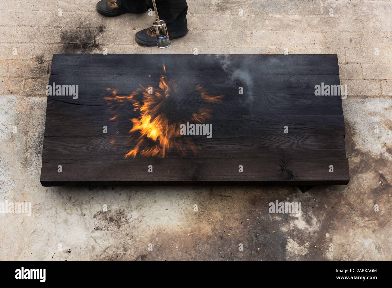 Ein Mann mit einer brennenden Fackel und Brennen ein grosses Stück eiche Erstellen von Flammen und Rauch, alte jappanese Shou sugi Verbot Technik. schwarz Holz- material. Gra Stockfoto