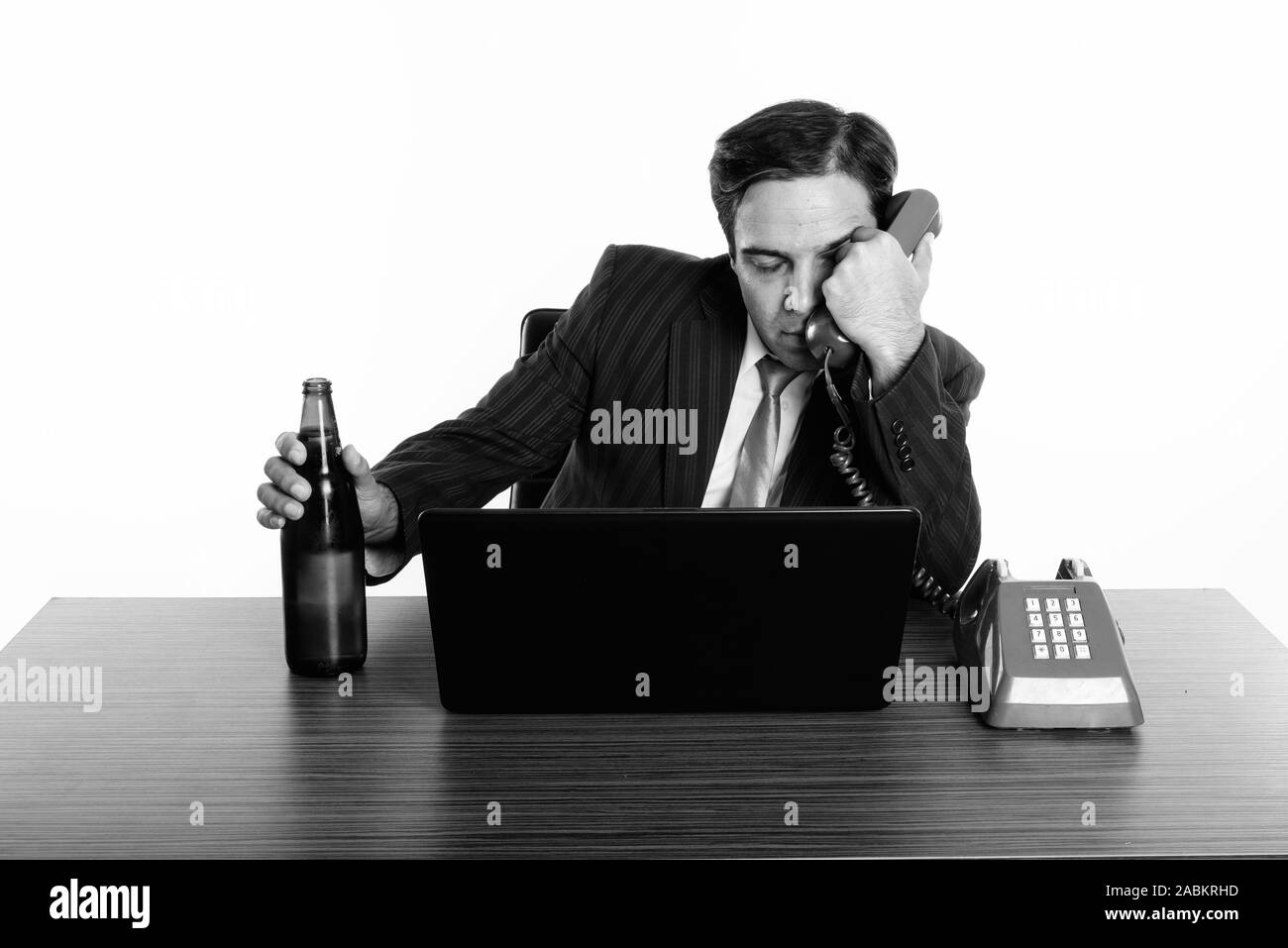 Persische Geschäftsmann auf der Suche betrunken Halten Sie Flasche Bier und alten Telefon mit Laptop auf hölzernen Tisch Stockfoto