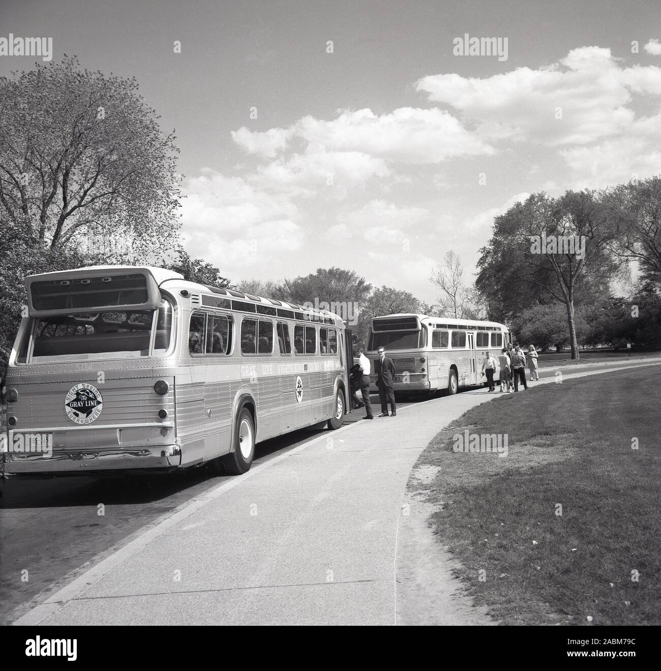 1950er Jahre, historisch, zwei Gray Line Reisebusse, geparkt an einer Straße neben einem öffentlichen Park, USA. Als führender Anbieter von Besichtigungstouren geht die Geschichte des Unternehmens auf das Jahr 1910 zurück, als Louis Bush begann, Touren durch Washington, D.C., mit einem renovierten alten, blau-grauen Mack-Truck anzubieten. Stockfoto