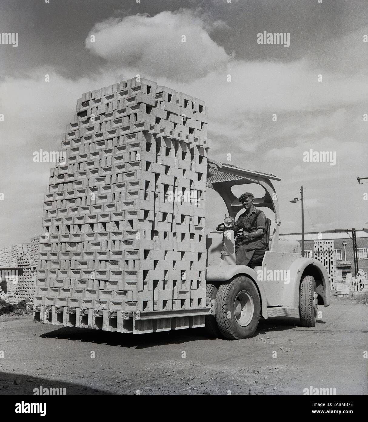 1950er Jahre, historisch, draußen in einem Depot bei der London Brick Company, ein männlicher Arbeiter in einem Gabelstapler, der eine große Ladung Lehmziegel bewegt, in Stewartby, Bedfordshire, England, Großbritannien. In dieser Zeit war die Ziegelei die größte der Welt und die Besitzer, die Familie Stewart baute ein "Modelldorf" für seine Belegschaft, mit Wohnungen, Sport und soziale Einrichtungen wie eine Schule, Shop, Bibliothek und Kirche. Stockfoto