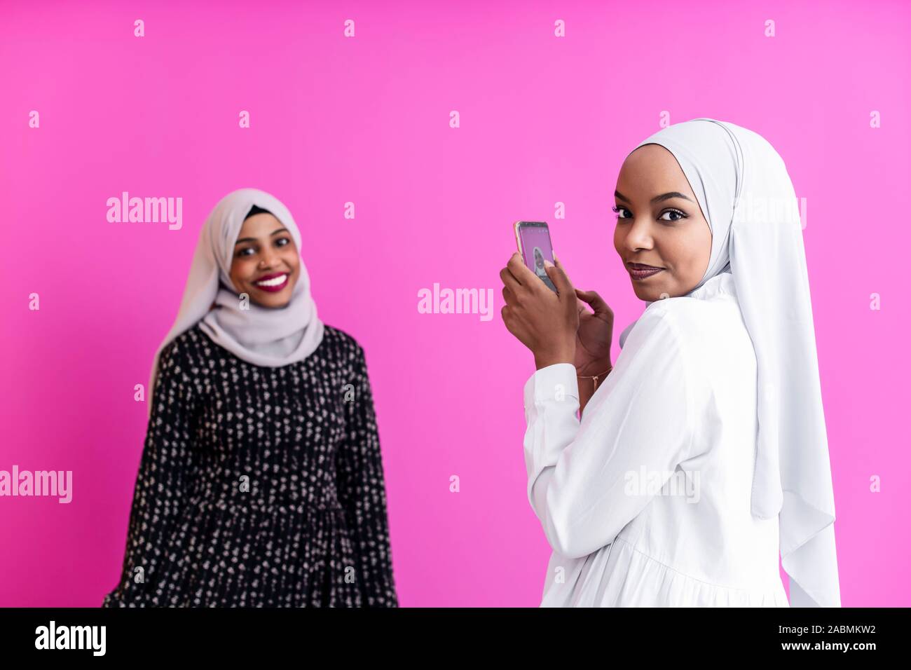 Porträt von zwei unterschiedlichen afrikanischen Kursteilnehmer Mädchen, Schal moderne muslimische Kleidung, Self Portrait With Phone gegen Kunststoff rosa Hintergrund Stockfoto