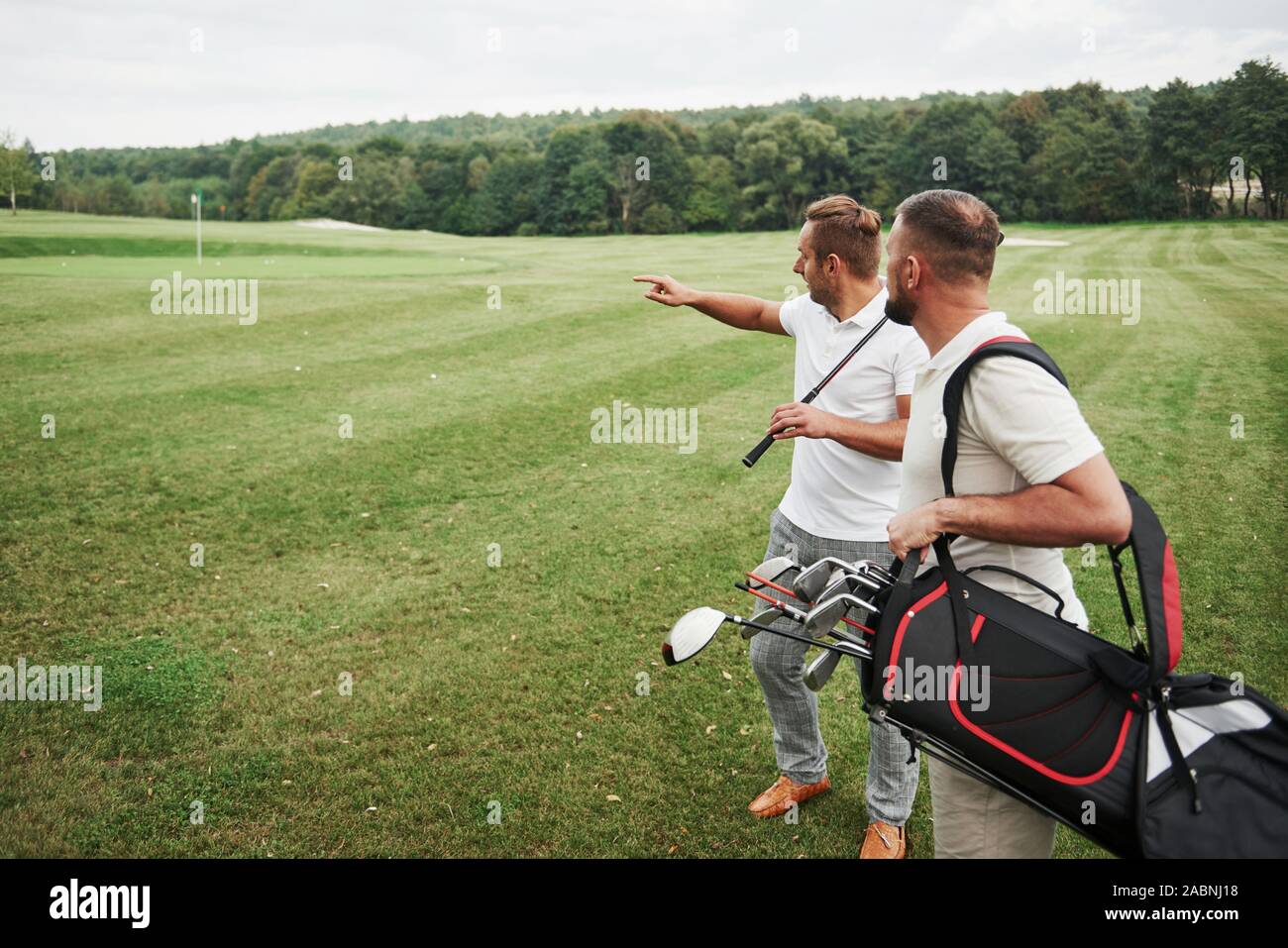 Zwei stilvolle Männer holding Taschen mit Vereinen und gehen auf Golfplatz Stockfoto