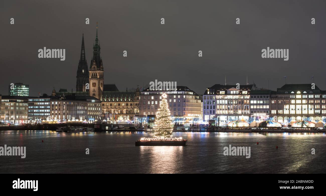 Hamburg, Deutschland. 28 Nov, 2019. Ein Weihnachtsbaum, der sogenannten Alstertanne, glänzt auf der Binnenalster. Im Hintergrund sehen Sie die Türme der Mahnmal St. Nikolai (l) und das Rathaus. Der Hamburger Buergermeister, Tschentscher (SPD) eingeschaltet, feierlich die Lichter auf den traditionellen Weihnachtsbaum am Abend. Credit: Daniel Bockwoldt/dpa/Alamy leben Nachrichten Stockfoto