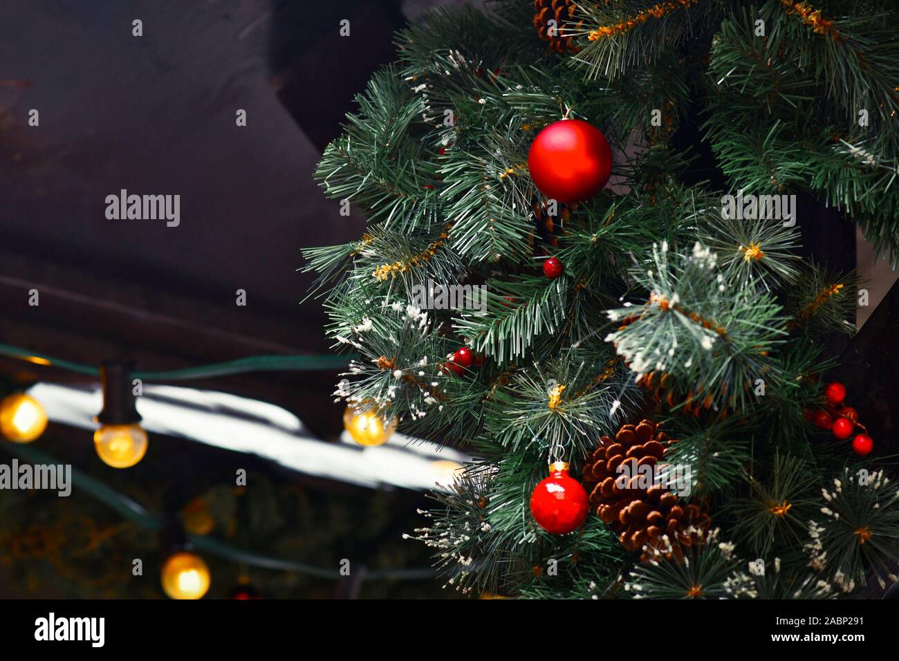 Weihnachtsbaum mit künstlichem Schnee mit Tannenzapfen und Red tree ornament Flitter und Lichterkette im Hintergrund bei traditionellen Weihnachten dekoriert Stockfoto