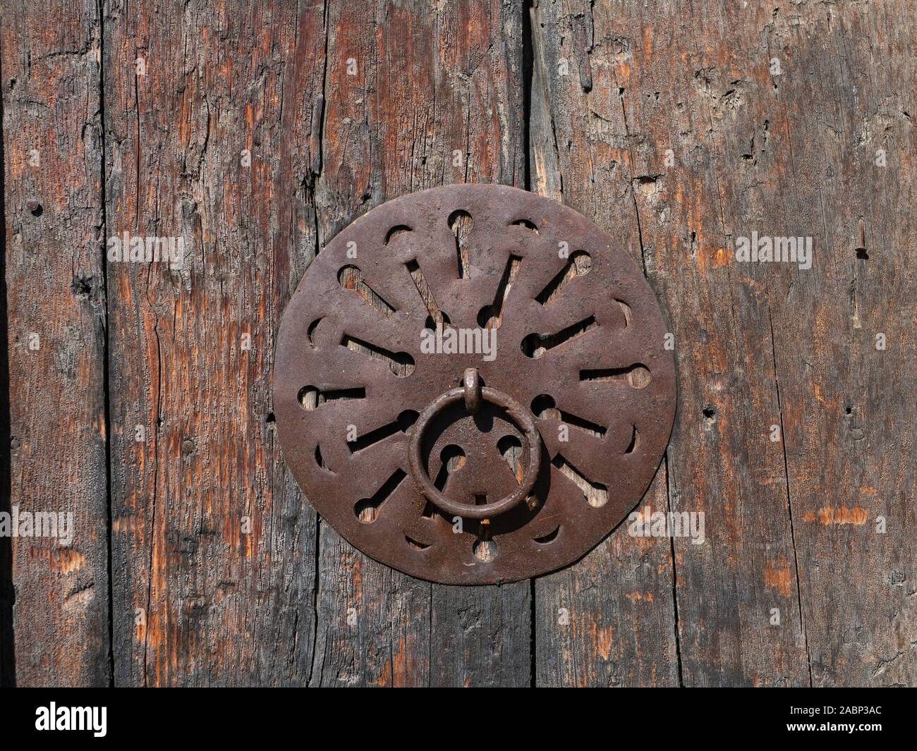Nahaufnahme von einem kreisförmigen Metall Tür ziehen mit dekorativen geometrischen Zuschnitte auf ein verwittertes Holz Tür montiert. Stockfoto