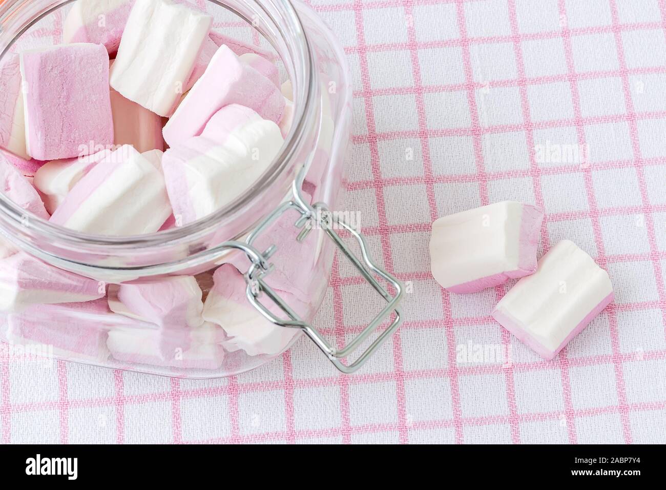 Weiß rosa Flauschige Marshmallows in einem Clip top Glas Glas auf einem karierten Tischtuch. Süß und lecker Essen im Winter. Close-up köstliche weiche Süßigkeiten. Stockfoto