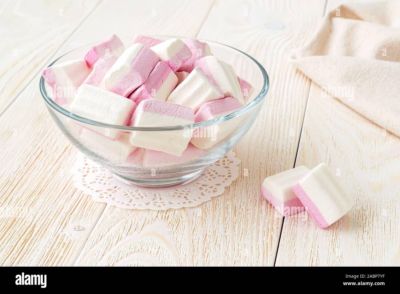 Weiß rosa Flauschige Marshmallows in einem durchsichtigen Glas Schüssel auf einen hölzernen Tisch. Süß und lecker Essen im Winter. Close-up köstliche weiche Süßigkeiten. Vorderansicht. Stockfoto