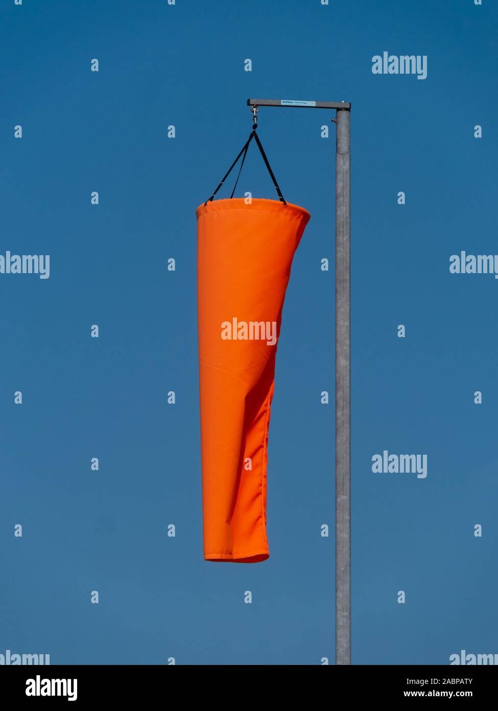 Neuen hellen orange Windsack herunterhängt, in Ruhe, immer noch kein Wind und Wetter mit blauem Himmel hinter sich. Stockfoto