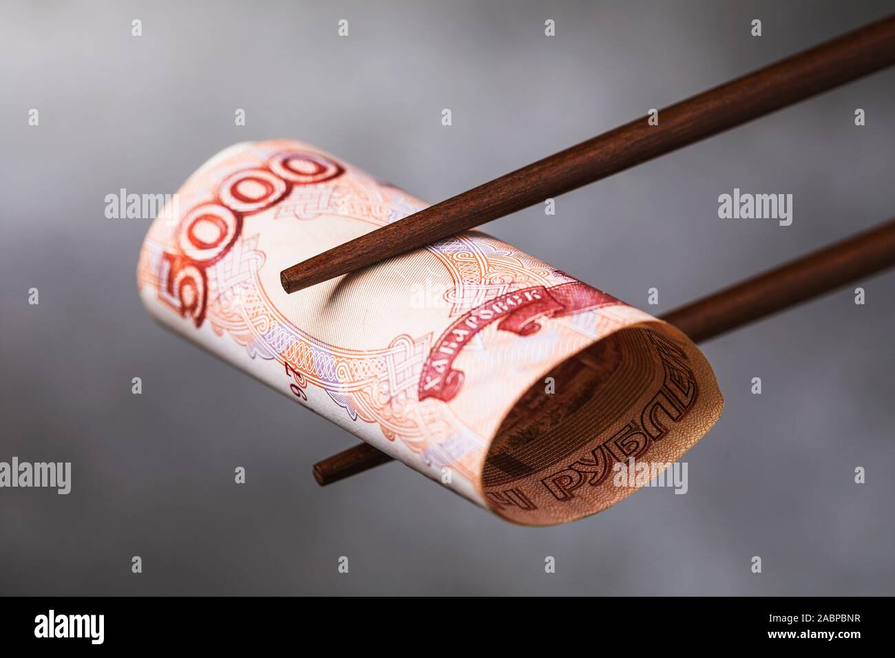 Chinese sticks halten fünf Tausend Rubel, close-up. Internationale Beziehungen zwischen Russland und China Stockfoto