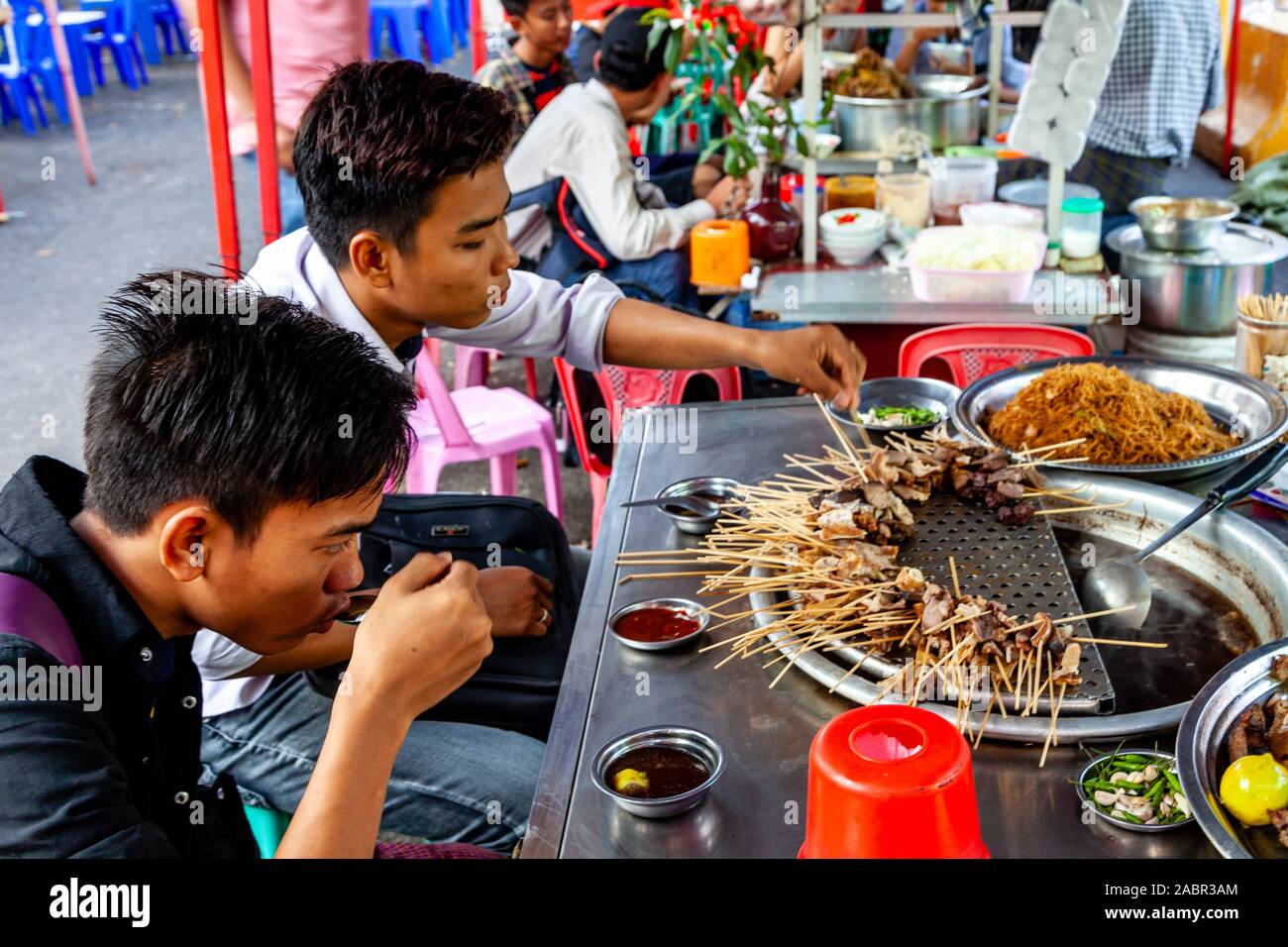 Zwei junge Männer essen Essen aus einem Stall in der Innenstadt von Rangun, Yangon, Myanmar. Stockfoto
